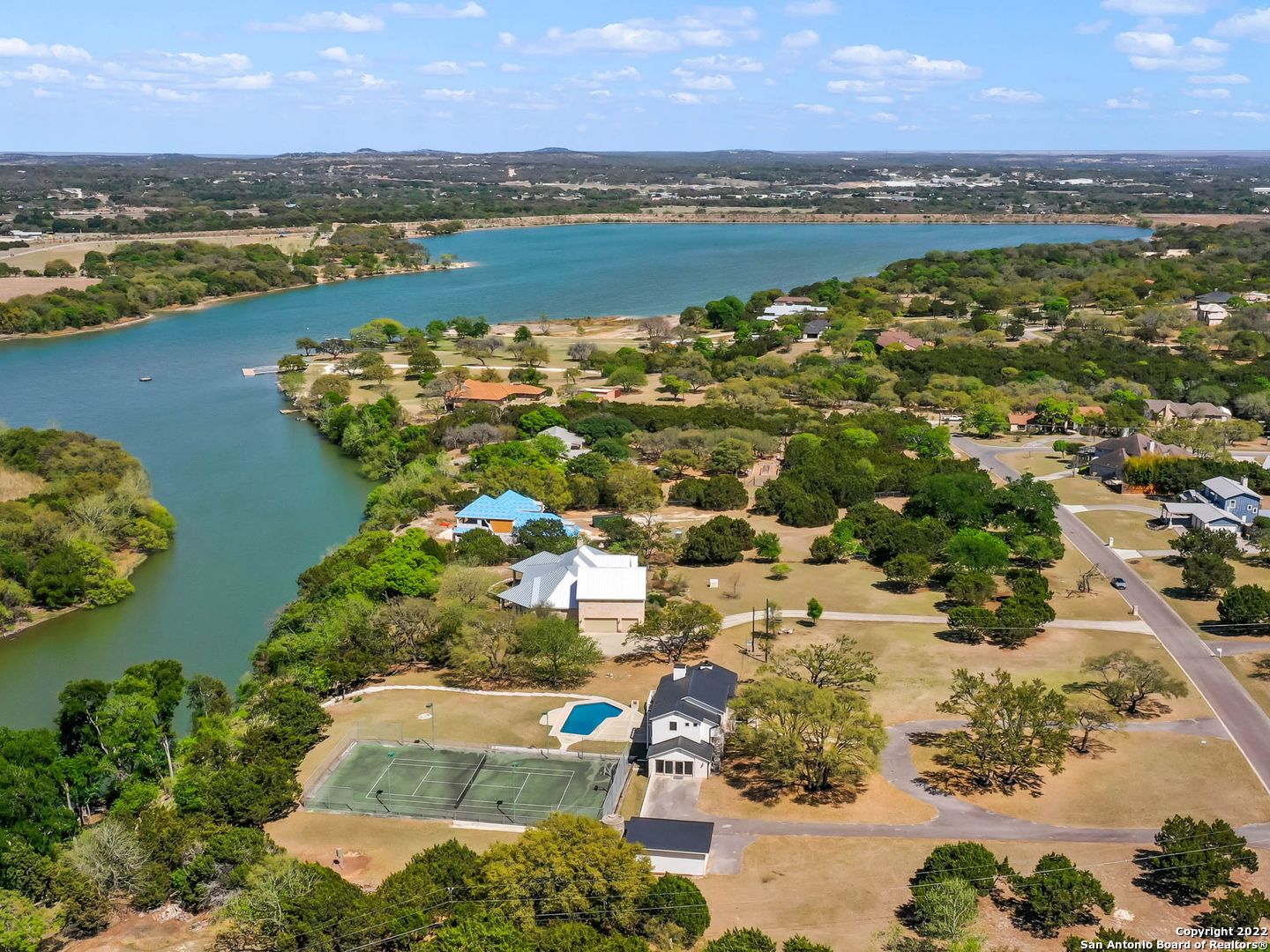 A truly unique getaway property with pristine waterfront, where panoramic lake and sunset views of Boerne Lake is your backdrop. Nestled on a rare grey lot, grandfathered with no HOA restrictions, totaling over 4 acres for unmatched lakefront living. Abundant natural lighting fills the home and floods the interiors with an exceptional floor-plan. Light-filled living with gorgeous hard wood floors, soaring cathedral ceiling and walls of windows for seamless indoor-outdoor living and a gourmet kitchen overlooking the outdoor oasis. A master retreat is found upstairs complete with a sun-filled spa like bathroom. At the lower levels leading outdoors are the remaining spacious guest bedrooms and an oversized game-room. Enjoy tranquility outdoors with a large covered wooden deck leading to a sparkling pool and full sized sports court. As one of the twelve properties in the entire subdivision with direct lake access, a flagstone walkway leads you down to your private 20 foot dock and flagstone hard-decking for multiple entertaining spaces. An exemplary offering with endless possibilities within Lake Country in Boerne.