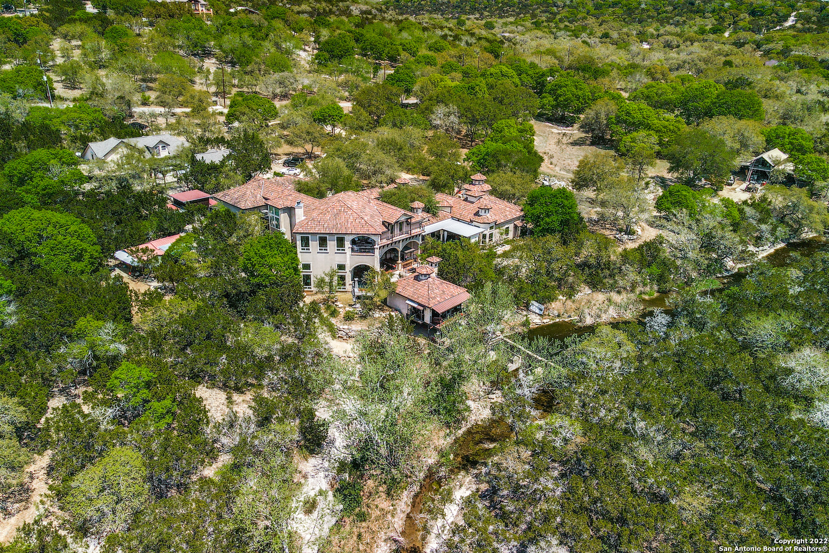 Own a Private Oasis in the Texas Hill Country situated along your very own spring fed, year-round creek! This Magnificent 2-story Mediterranean-style Estate sits on 10 acres of Hill Country in the Heart of Grey Forest with picturesque 360-degree views of the surrounding hills and total privacy in your backyard Hill Country paradise is only 30 min to the San Antonio International Airport and 2 hours to Austin. Enjoy the convenience of being close to 1604, I-10, and all of the shopping at The Rim & La Cantera. The open concept layout offers natural light showcasing a neutral color palette, crown molding, arched entryways, high level finishes such as alabaster, hand scraped wood and travertine floors, marble statues throughout and floor to ceiling stone fireplaces. Plenty of room for outdoor entertaining with large front & back patios, a cabana and two outdoor kitchens overlooking the water. The chef's kitchen is equipped with custom maple wood cabinetry, quartz countertops, a spacious walk-in pantry along with a Butler's pantry. The main-level master suite features tray ceilings with a sitting area overlooking the creek and private patio access. You are greeted by a grandiose statue in the master bathroom and the spaciousness of a dual vanity, an oversized marble garden tub with a fireplace and a beautiful curved walk-in shower. Upstairs, each bedroom has its own private balcony overlooking the creek and a media room perfect for game night or your own private theater. The Main House also featured a 4-car garage with separate stairway to the second floor.  In addition to the Main House, you will enjoy 2 separate Guest Homes on the property as well as an Equipment Barn and three-level deck overlooking the creek and dam. Owner financing available! New asphalt has been added to driveway!