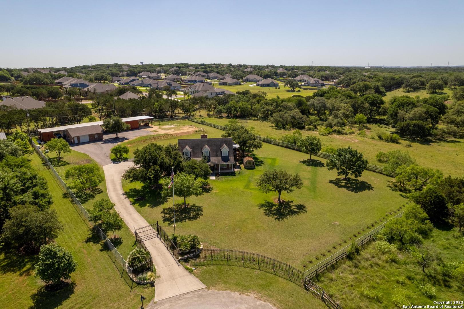 The property's magnificent location is key to its value. This 1.86-acre estate exists in Comal County, outside the city limits of Garden Ridge & San Antonio, on a dead-end, cul-de-sac street with easy access to nearby shopping, dining, & major hwys, IH35, Loop 1604 & 410. Beautiful country landscape with gorgeous greenery, mature trees, deer roaming gently and longhorn steer grazing nearby. The dynamic location, the peaceful views, & the private, secluded lot make this property outstanding! Oh, by the way, No city taxes & No mandatory HOA! The rectangular-shaped, level lot is completely fenced with six-foot chain link fencing & accentuated with secure wrought iron fencing & gated entrance with a twelve-foot wide electric gate with remote, and, or, keypad access.  The long concrete driveway welcomes you to a two-story, all-brick home with covered front & back patios & an attached two-car garage with side entry. Built in 1992 with 2394 square feet, the home features beautiful hardwood flooring, a cathedral ceiling, a wood-burning fireplace, an eat-in kitchen with an island, a breakfast bar, and a separate dining area. Upstairs, with its own private entrance, is a guest suite that includes a large bedroom, a full bath, & huge walk-in closet. A perfectly planned eat-in kitchen and an inviting living area, a large pantry for extra storage & awesome views off the covered balcony. Flexible floor plan; can be a three-bedroom, two-bath home with two kitchens. There is a detached workshop or oversized garage with an overhead electric door. Two additional carports for open, covered parking. The seller recently installed a Generac, 24KW, home backup generator with a 250-gallon propane tank- only six months old. The water well is on-site with a chlorinating system. The downstairs kitchen features reverse osmosis for drinking water. There is a 2500-gallon water storage tank which is set on a concrete, heavy-duty pad. Also included is a 1000-gallon round concrete, conventional septic tank. With your own water well & septic tank, you'll have no water bills! City utilities, high-speed internet, & cable are available. Private trash services. U.S. mail is delivered daily. Two ac/heat pump systems were installed in the home about a year and a half ago. A new roof is to be installed.  And, lastly, there are two RV hookups, both under a cover with 240V electric service. Must see to appreciate!