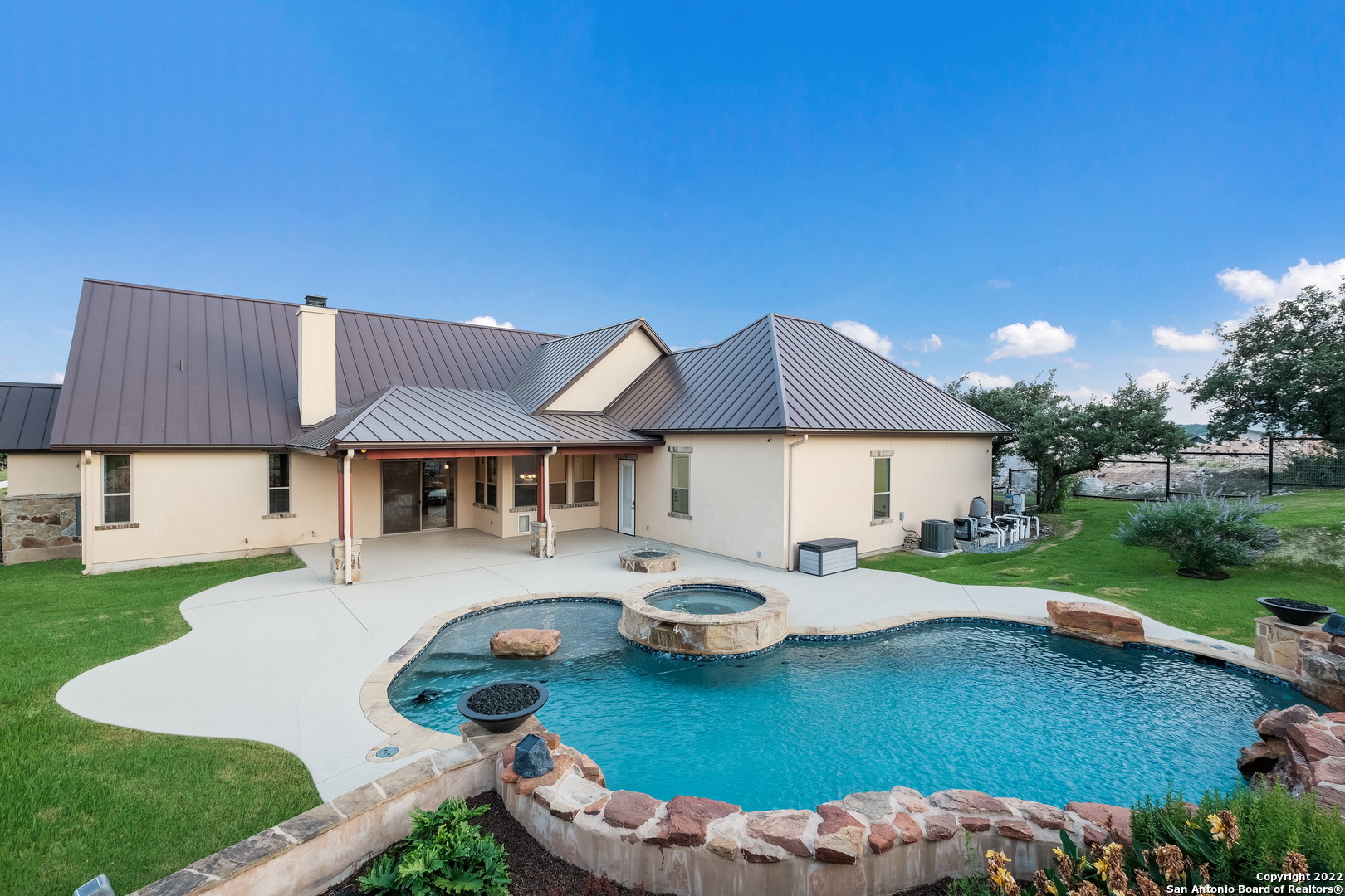 A meticulously maintained Texas Hill Country home features a luxurious Keith Zars Custom built in-ground pool with a luxury spa located within the prestigious Canyons at Scenic Loop! (KZP Lifestyle Protection Plan included & Paid in full until 2023). This 3 bedroom, 5 bath two story home boasts a captivating backyard oasis with breathtaking views of the evening sunset. The beautiful stone and stucco exterior features a metal roof that complements the well manicured front/back landscaping. This home provides plenty of parking space with a 3 car garage and attached oversized workshop that includes a climate control atmosphere w/ a half bath, LED lights, ceiling fans, and 13' ceilings. The open concept layout welcomes the seamless flow from the living room to the chef's kitchen and the spacious dining room that overlooks the gorgeous pool and spa out to the backyard. Custom upgrades throughout the home include the stone rock gas fireplace, travertine stone flooring, and upgraded carpet in the en suite bedrooms, walk-in luxury showers in primary/guest suite on main level.  Open study w/ custom built-in bookshelves and matching baseboards throughout give this home the modern, but rustic look. The thoughtfully designed Knotty Alder cabinetry looks gorgeous in the kitchen w/ the granite fusion countertop island w/ surrounding countertops appointed with leathered granite, top-rated stainless steel appliances and black granite double sink w/ touchless faucet give this gourmet kitchen its finishing touch. The upstairs features the amazing media room equipped with the top-of-the- line surround sound and 110" movie screen along with all 4K video and receiver components, professionally installed and designed by Magnolia Audio/Video. Off of the media room, there is large game room or (use it as flex space), and spare third bedroom with a separate bathroom that includes an oversized soaker tub. Too many upgrades to list, please see property feature list in MLS additional information section. Easy access to Shops at La Cantera, The Rim, restaurants, and major highways IH-10/1604. Schedule your showing today and make this your dream home!