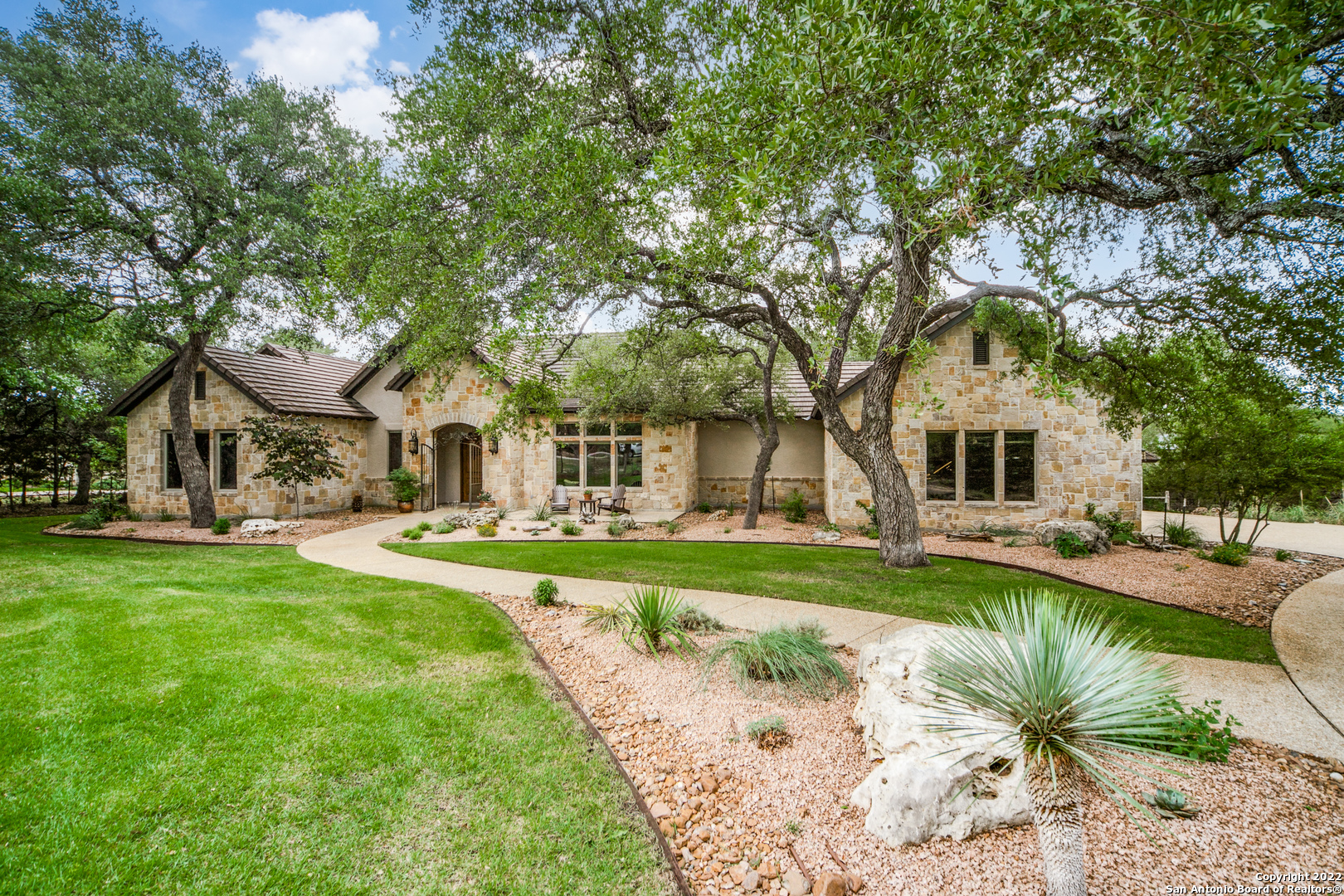 Find an escape from the hustle and bustle of the city with this gorgeous Hill Country gem. Nestled on an expansive lot with a bluff view and mature trees, this stunning countryside retreat's stone and stucco exterior opens to reveal a stately interior filled with quality craftsmanship. Rustic charm is found throughout the home's open floor plan in the form of high ceilings with exposed wood beams, tile and hardwood floors, arched doorways and exquisite mouldings. Located next to the grand double door entry is the formal dining room. The spacious family room features a patio access, surround sound wiring and a stone fireplace that extends to the crest of the cathedral ceiling. Take your culinary abilities to new heights in the spacious island kitchen, complete with granite counters, tile backsplash with a mosaic centerpiece, stainless steel appliances, a casual dining nook with bow windows and pendant lighting suspended over an eat-in breakfast bar. Boasting a tray ceiling, bow windows and a walk-in closet, the relaxing primary suite exudes an aura of refined elegance. Equipped with dual vanities, an inset whirlpool tub and separate shower, the primary en suite bath is perfect for melting away stress after a long day. Other distinguishing features include a private office and reading room with French doors and custom built-ins, as well as well-appointed secondary bedrooms. Just behind the home is an incredible outdoor paradise, which contains a covered patio with an outdoor fireplace, summer kitchen and patio speaker wiring, a Keith Zars pool and waterfall, plenty of mature trees and a detached Casita of 720SF, which includes a large living area, and an additional bedroom and bath. With the casita this house is a total of 4428SF priced at $375/SF. Whole house generator ($26,000) installed in 2021. Social country club membership is available.
