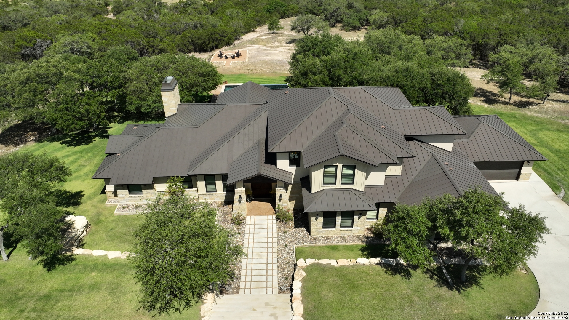 Better Than New!  Sensational Hill Country Masterpiece on 15 +/- acres.   Upon first step into the foyer, the soaring ceiling, brilliant architectural design, and gorgeous hardwood flooring create an instant WOW factor. Two Master Suites on first level! Recent rehab with all new exterior & interior paint, new carpet. 5 Total Bedrooms, 5 Full Baths, 1 Half-Bath, 4 Car Garage.  Patio opens from owner's suite moving along to the main covered patio with vaulted ceiling and wood beams continuing to a large Outdoor Kitchen. Serene faux edge pool with Spa overlooks acreage.  The open and inviting custom-designed floor plan includes a warm, welcoming interior which is awash with natural light and incorporates a separate dining room, two expansive living areas, flow-through living/dining area. The refined, timeless style is well-executed to complement, and not compete against the alluring outdoor elements, overlooking the surrounding valley.  Key features of this house include windows with plantation shutters, wide wood & iron staircase with storage underneath and beamed ceilings. Designed for gatherings and casual entertaining, this gourmet, eat-in kitchen  has been beautifully maintained and features commercial-grade appliances, electric and gas ovens, granite countertops, stone backsplash, stunning kitchen island, custom-made cabinets, decorative pendant lighting, large walk-in pantry, built-in microwave, gas range and wine fridge.  Spread out in the opulent downstairs owner's suite that comes complete with a luxury en suite bathroom, his-and-her walk-in closets and impressive valley views. A true oasis, the master bathroom is akin to a 5-star hotel and features a spa shower, deep Copper soaking tub, his-and-her vanities, marble countertops, and slate flooring.  Second master bedroom is a perfect mother-in-law suite complete with en suite, walk-in shower, walk-in closet, custom cabinets and slate floor.  Two of the three bedrooms upstairs feature phenomenal en suites each with stone and granite floors and vanities.  Three study areas, with soapstone work counters, are tucked strategically throughout both levels.  Wet Bar is set aside by the downstairs half-bath awaiting your pristine wine selection.    Adding to the home's charm are wood floors throughout the main living spaces. You will find System updates includes three upgraded HVAC systems, efficient furnace, smart security cameras, smart sound system, smart lighting system, smart locks and garage-door openers, Wi-Fi enabled thermostats, Energy Star appliances, built-in stainless Refrigerator/Freezer and high-efficiency kitchen appliances which makes it an ideal turn-key solution. Perched on the cusp of the property lined with historic live oaks is the resort like backyard! 1/2 mile walking trail carved throughout the wooded acreage accessible from the back yard.  View the vast dry-creek bed enshrined in limestone walls.  Outdoor Kitchen boasts built-in barbecue, built-in cooler, cook top, pool and hot tub, beautifully manicured lawn, large grassy area for yard games, well-established trees and shady trees. Take advantage of the best suburban living around! Simply ideal for year-round entertaining. Ideally located in an incomparable Bexar County neighborhood. A short drive to mixed-use shopping and dining areas. You have all the amenities you would like a short distance from home. Appreciate the benefits of a spacious 4-car attached garage. Plenty of room to park and enjoy top-rated Comal schools.  Be prepared for 'love at first sight'. Schedule your private tour today.