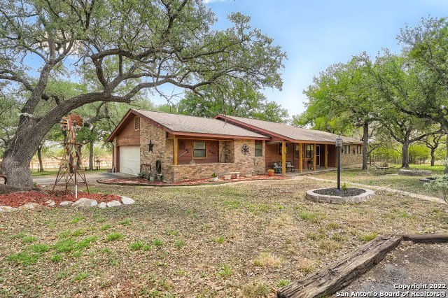 This custom 1 story home sits on 2 acres in NW San Antonio and is surrounded by mature trees and a natural landscape - a beautiful and hard to find setting to call home - country living with city conveniences - and no city taxes or mandatory HOA!  The brick and cedar siding as well as the other cedar accents on this home fit perfectly into the country surroundings. You're greeted by a covered porch at the front door, where you can enjoy a morning cup of coffee or an evening drink.  As you enter, you'll see the large living room with a connected dining room, and a brick fireplace that can be enjoyed by both areas.  There's also a wet bar in the living area which comes in handy for entertaining.  The galley kitchen has plenty of counter and cabinet space, stainless steel appliances, and a nice sized walk-in pantry.  The kitchen herb garden window overlooks the front yard, allowing you to enjoy the outdoors while preparing your meals. The breakfast area off of the kitchen allows plenty of space for shared meals or playing games with family and friends.   The utility room and half bath are just past the kitchen and lead to the oversized 2 car garage.  They don't often make garages like this anymore - there's room to park your car(s) as well as store your tools, holiday decorations, outdoor equipment etc. - there's even an extended space for your extra fridge and/or freezer.  On the other side of the home you'll find a full bathroom with a long single vanity, and a separate toilet and shower area.  The nicely sized secondary bedrooms are located down this hallway, as is the large primary bedroom. This room has a walk-in closet, and en-suite bathroom with a single vanity and shower.  There's access through the primary bedroom to the large backyard deck - another outdoor space to enjoy!  Host gatherings or simply enjoy the space yourself - either way, you'll love being surrounded by nature, and all this yard has to offer.  There is an additional space to enjoy off of the living room - an enclosed porch/Florida room that runs the length of the living and dining areas.  Another place to sit and enjoy the outdoors, but without the heat or cold of the season.  The outside of the home has several notable items - 2 year old roof, oversized, concrete, covered RV parking, a front circular drive and additional parking areas to the side, allowing for plenty of space to park extra vehicles, boats, trailers etc., storage shed, well and septic systems, and has gutters.  While there is no mandatory HOA, it is a deed restricted area with a voluntary HOA if you choose to join.  Close to area shopping, restaurants, grocery stores, Northside ISD schools, highways and other conveniences.