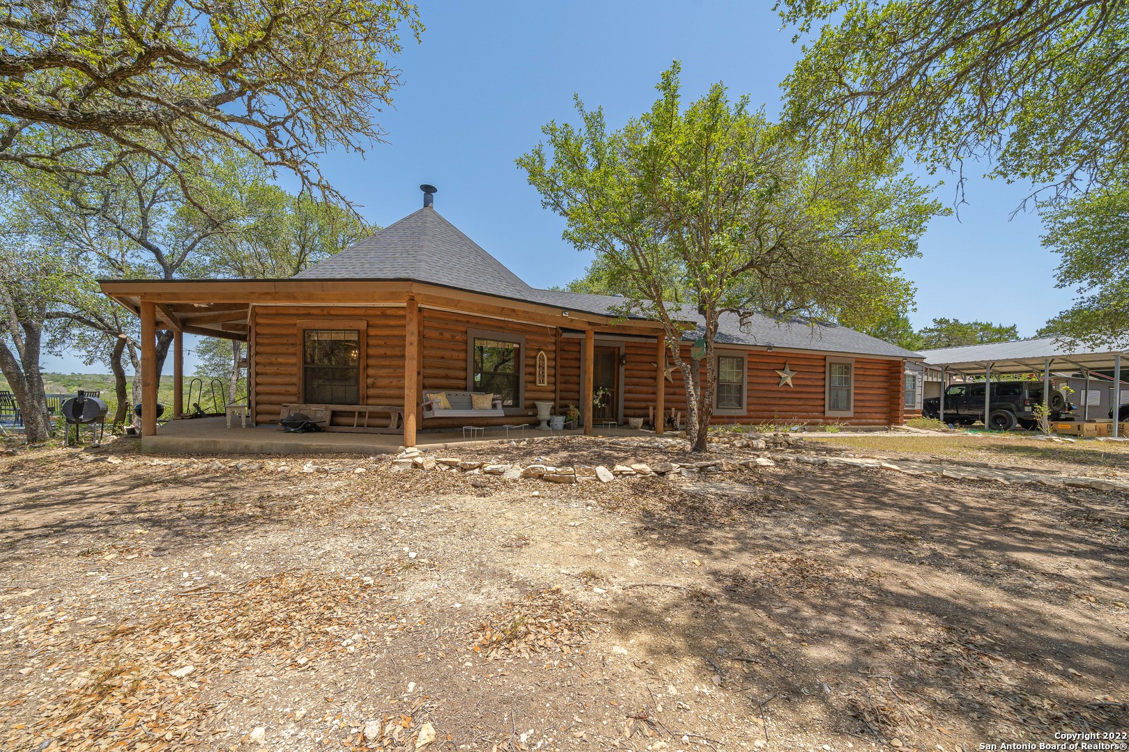 Very unique and cozy log cabin on fenced 6.96 acres.  Amazing Hill Country views.  Open floor plan in the octagonal living/dining/kitchen area.  Rock fireplace in the living room and a beautiful Heartland Sweet Heart Stove, wood burning, in the center of the kitchen.  Kitchen counters were updated with quartz countertops. Main bathroom updated with frameless glass shower and a granite top corner cabinet, flooring was updated with tile.  Master bath features a wooden soaking tub. Huge master suite that leads to an office/study/sunroom.  Spiral staircase leads to a spacious loft area.  HVAC system features whole house oxidation system to neutralize air.  A breezeway leads to a 2 car garage with a half bath.  Additional 2 car covered carport.  Workshop, storage shed.  2400 gallon water tank and a deep well.  Lots of fruit trees.  Electric gate at the entrance.  The log cabin is custom build with 9" logs.  All screws, no nails.  Roof recently replaced in early 2021.  Hill Country living at its best yet close to Boerne, San Antonio and all shopping conveniences.  A MUST SEE!