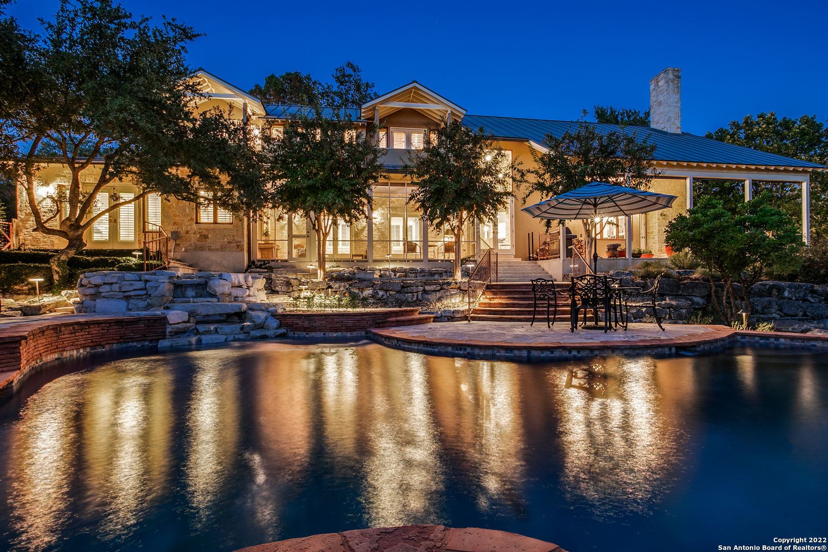 Designed by renowned architect Joe Stubblefield, this impeccable split-level home offers access to the incredible luxury found in Sendero Ranch. Immediately past the grand French entry doors embedded into a stunning limestone exterior is a unified living space with a 2-story vaulted ceiling, anchored around an impressive stone fireplace flanked by floor-to-ceiling windows. Hardwood floors, stone accent walls and arched doorways can be found throughout the spacious interior. Granite counters, tile backsplash, stainless steel JennAir appliances and pendant lights over the breakfast bar provide the gourmet kitchen with a sense of refinement. Plantation shutters, custom  millwork, dual walk-in closets and a remarkable en suite bath with dual vanities, an open shower and a soaking tub embedded into a decorative tile backsplash with ornate mosaic accents allow residents to lavishly relax in the private primary suite. Wrought iron spindles guide the stairs up to a lofted space, which then leads to a guest suite with a kitchenette and two additional secondary suites. Balconies and a screened porch with Redondo tiles overlook the private backyard retreat, complete with a covered flagstone patio with outdoor fireplace, which extends down to a sparkling pool with  waterfall, spa, mature trees and xeriscaping, as well as well-maintained landscaping.