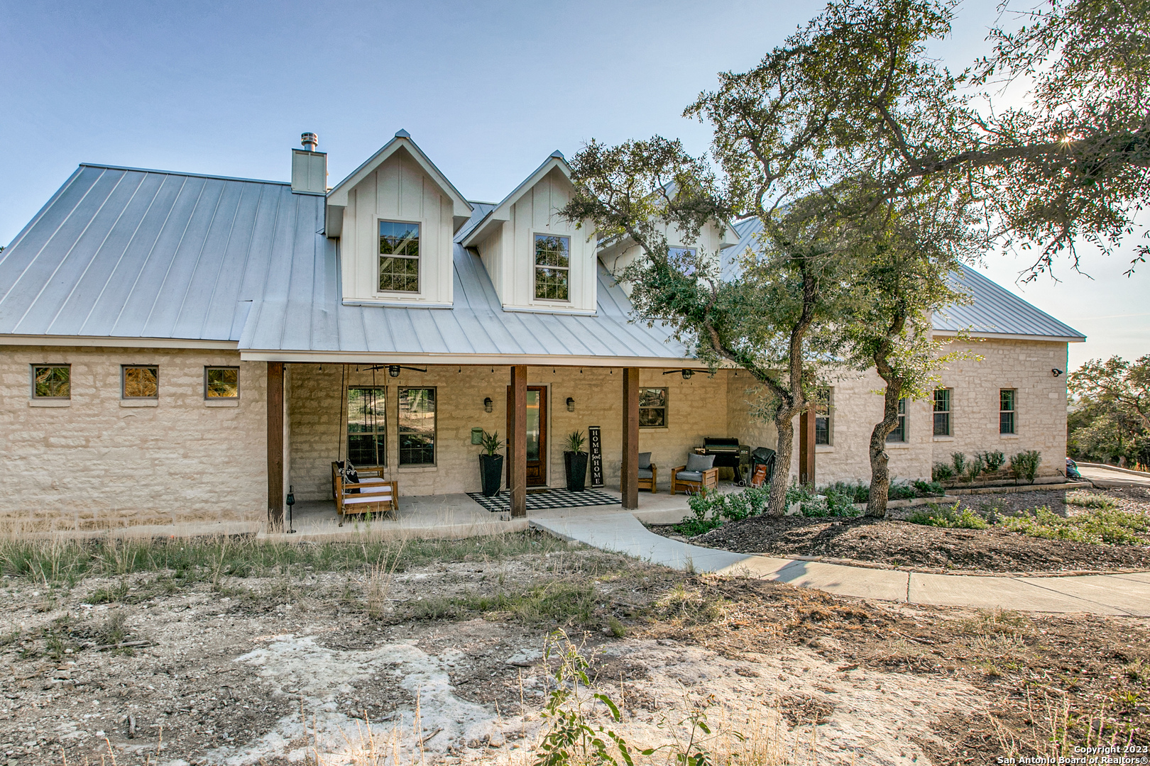 This spectacular custom-built Farmhouse is located in the beautiful Texas Hill Country with incredible views, in the gated community of Dancing Bear Ranch. It's absolutely amazing and a true stunner! Only minutes from Medina Lake, you have access to your own private lakeside park, exclusive boat launch, a fishing pier & residents only gate access. This one-of-a-kind 3,650 sq.ft. farmhouse design features 4 bedrooms and 3 baths, 20' vaulted ceiling in the living room, 18' vaulted ceiling in the downstairs master suite, and standard 10' ceilings throughout. This beautiful two-story layout features a spa style master bath with 2 rain shower heads and walk-in shower, his and her sinks and granite counter tops, plus two oversized walk-in closets. There are two very spacious bedrooms upstairs as well as a grand-sized full bathroom with granite counters, double sinks and mirrors giving everyone their own space. An upstairs office/workstation sits adjacent to the upper-level bedrooms and an open multi-use 26' X 25' bonus space that is perfect for a game room, home gym, or a private home theater. Plus, it has a spectacular view of the Texas Hills! There are exquisite custom home finishes throughout the home, from the Brazilian "Ornamental White Ice" granite in the kitchen and baths with complementary high-end fixtures you would only expect in your custom home. You will find plenty of storage in the custom cabinets throughout the home and plenty of closet space! Upscale super-size side by side refrigerator/freezer in stainless steel, two ss ovens, a built-in microwave and a coffee bar that makes this kitchen a great place to entertain or cook to your heart's content. A kitchen bar provides seating space for guests or family, a huge walk-in pantry with custom shelving and an offset dining room that is surrounded with views of the outdoors, all perfect for entertaining. An open floorplan throughout gives you room to breathe and includes the large living area anchored with a 20' Texas limestone brick fireplace and rustic hand-hewn solid wood beam mantel. Wood tile floors flow throughout the downstairs level with a beautiful wood staircase inviting you upstairs. Separate mudroom and laundry spaces keep this home open and high functioning. The three-car/truck oversized garage is finished with epoxy floors and is insulated with finished and painted walls- perfect for adding a home gym and still having plenty of space to park. A covered patio with an elevated terraced lawn is just the place to take in the view and relax. This great looking and spacious home sits on a 2+ acre lot with no rear neighbors and offers plenty of privacy! There is ample usable land as cedar was cleared to make room for animals and outdoor play. This homesite offers exclusive Texas hill country views, plus the peace and quiet you would expect in a home that truly offers Texas Living at its Finest. Come and fall in love with your future home!